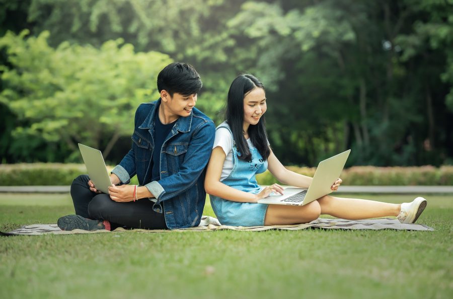 Thai man and girl sitting in park with laptops